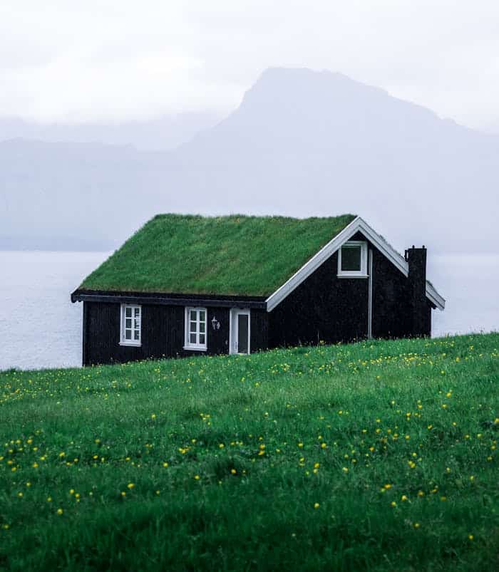 Charming black wooden house with a grass roof in the tranquil Faroe Islands landscape.