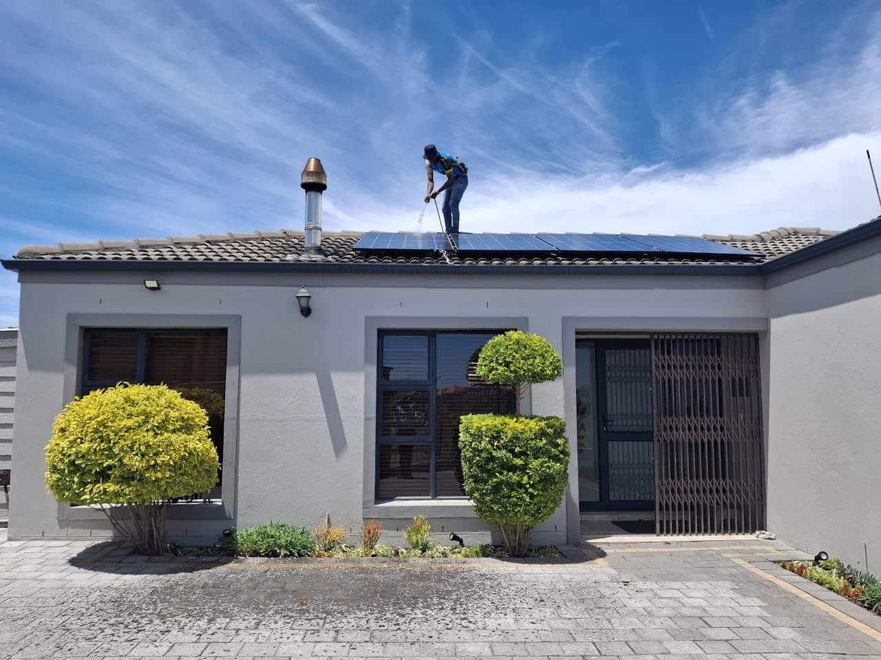 A person maintains solar panels on a house roof under a clear blue sky.