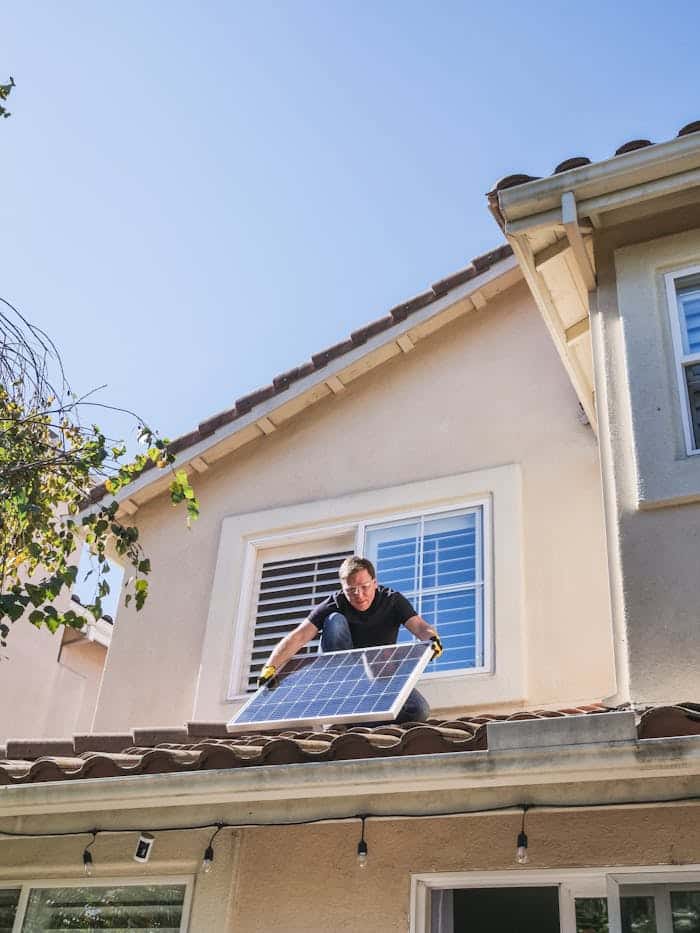 A worker installs a solar panel on a residential rooftop, showcasing renewable energy technology.